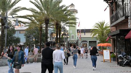 Visitors walk through the Disney Springs shopping, dining and entertainment complex, Tuesday, June 16, 2020, in Lake Buena Vista, Fla. Disney Springs reopened as part of a phased reopening during a new coronavirus pandemic, which included limited parking and entrances, temperature screenings prior to entry, face coverings required for guests ages 2 and up and social distancing. (Phelan M. Ebenhack via AP)