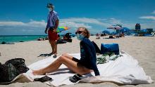 Diane, a nurse from Houston, Texas, sunbathes at the beach next to her husband, both wearing facemasks, in Miami Beach, Florida.