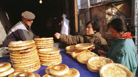 Un hombre uigur vende pan plano tradicional a las mujeres que compran en la calle Xinjiang de Beijing en 1999.
