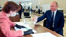 Russian President Vladimir Putin shows his passport to a member of an election commission as he arrives to take part in voting at a polling station in Moscow, Russia, Wednesday, July 1, 2020. The vote on the constitutional amendments that would reset the clock on Russian President Vladimir Putin's tenure and enable him to serve two more six-year terms is set to wrap up Wednesday. (Alexei Druzhinin, Sputnik, Kremlin Pool Photo via AP)