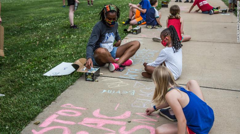Children writing phrases "Stop Racism" and "Black Lives Matter" on the sidewalk with chalk during the march. 