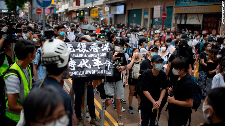 Passers-by and protesters gather in Causeway Bay, Hong Kong. A protester is seen carrying a flag that says &quot;Liberate Hong Kong, revolution of our times,&quot; an act that could now be considered a crime under the city&#39;s new national security law.