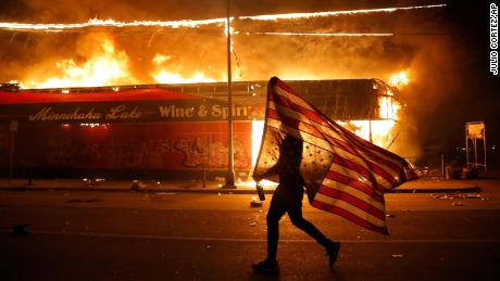 A protester carries a US flag upside down, a sign of distress, next to a burning building on May 28, 2020, in Minneapolis. 