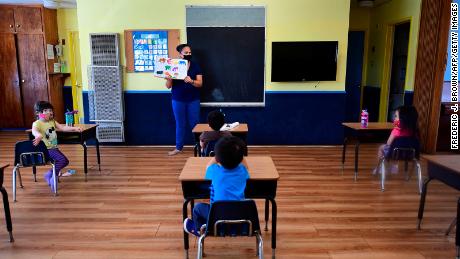 Instructor Chablis Torres (C) reads to children in a pre-school class, wearing masks and at desks spaced apart as per coronavirus guidelines during summer school sessions at Happy Day School in Monterey Park, California on July 9, 2020. - California Governor Gavin Newsom says the reopening of California schools for the coming school year will be based on safety and not pressure from President Donald Trump as California sets records for one-day increases in COVID-19 cases. (Photo by Frederic J. BROWN / AFP) (Photo by FREDERIC J. BROWN/AFP via Getty Images)