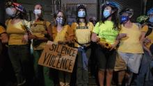 Women with interlocking arms stand with their backs up against a fence blocking access to the entrance of the federal courthouse in Portland, Ore., on July 19, 2020. (Photo by Alex Milan Tracy/Sipa USA)(Sipa via AP Images)