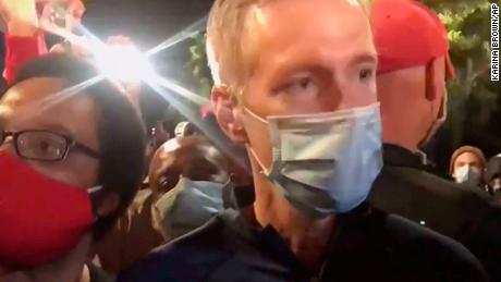 In this image made from video released by Karina Brown, Portland Mayor Ted Wheeler, right, stands at a fence guarding a federal courthouse as tear gas drifts by early July 23, 2020, in Portland Oregon, during another night of protest against the presence of federal agents sent by President Donald Trump to quell unrest in the city. (Karina Brown via AP)