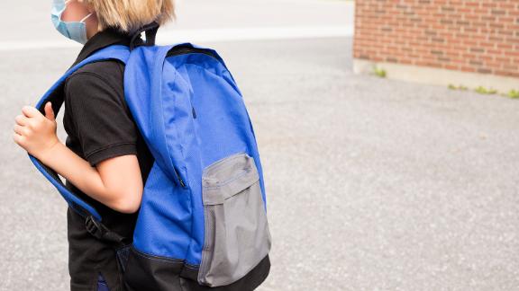 Little blond schoolboy wearing mask during corona virus and flu outbreak. School kid cough. Little kid wears blue backpack,breathes through mask, going to school.Back to school concept after reopening