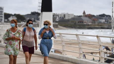 Women wearing masks walk along the seafront in Quiberon after a nighttime curfew was imposed on local beaches.