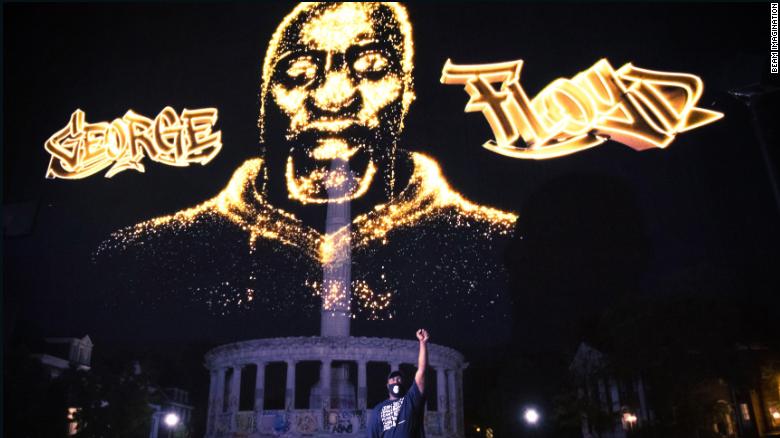 Rdoney Floyd stands in front of a hologram honoring his brother as it is projected over the Robert E. Lee statue in Richmond, Virginia, during a private event on July 27.  CNN obscured portions graffiti on the statue that contained profanity. 