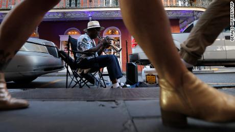 A musician plays his trumpet as pedestrians walk by on Royal Street in the French Quarter of New Orleans, Thursday, July 9, 2020. A sharp increase in COVID-19 cases and hospitalizations is forcing bars in the good-time-loving, tourist-dependent city to shut down again just a month after they were allowed to partially reopen. (AP Photo/Gerald Herbert)