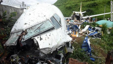 People stand Saturday by the debris of the Air India Express flight that skidded off a runway while landing in Kozhikode, Kerala state, India.