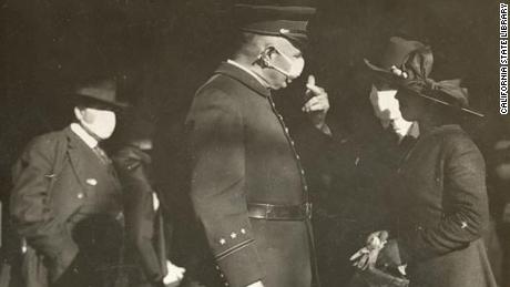 A San Francisco police officer talks to a couple about wearing masks in 1918. The man is wearing a mask but the woman is not, prompting a warning from the officer.