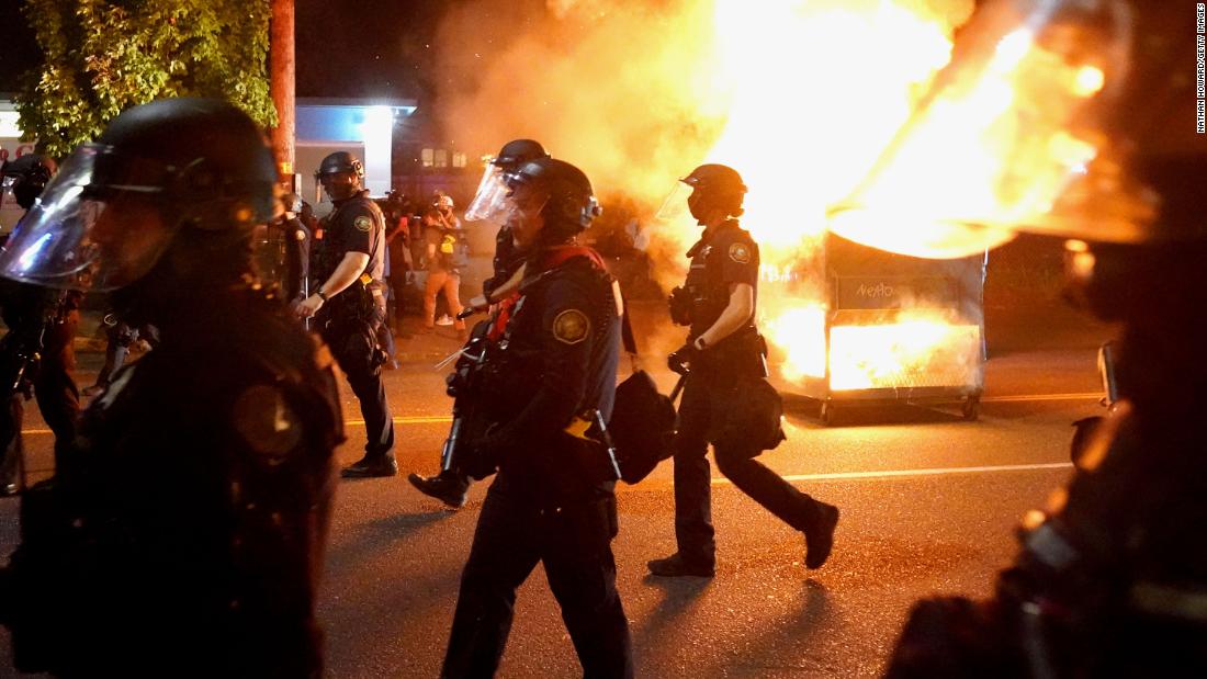 Portland police walk past a dumpster fire while dispersing a crowd of protesters on August 14.