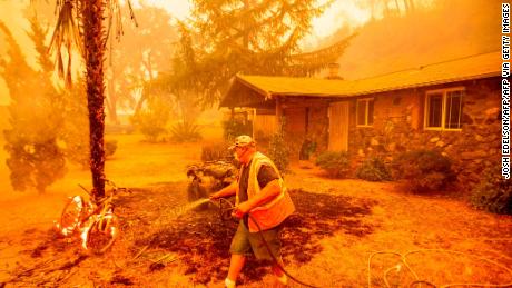 A resident hoses down a burning bicycle and tree as the Hennessey Fire approaches a home in Napa, California. 