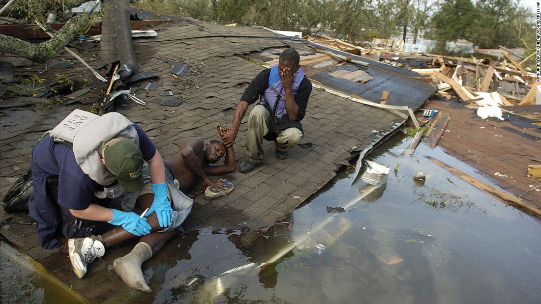 Paramedic David Mitchell examines Greg Farteberry on the roof of a destroyed home in New Orleans as Farteberry&#39;s friend Eric Charles holds his hand. Farteberry broke his ankle during the storm and spent the night on the roof until he was rescued.