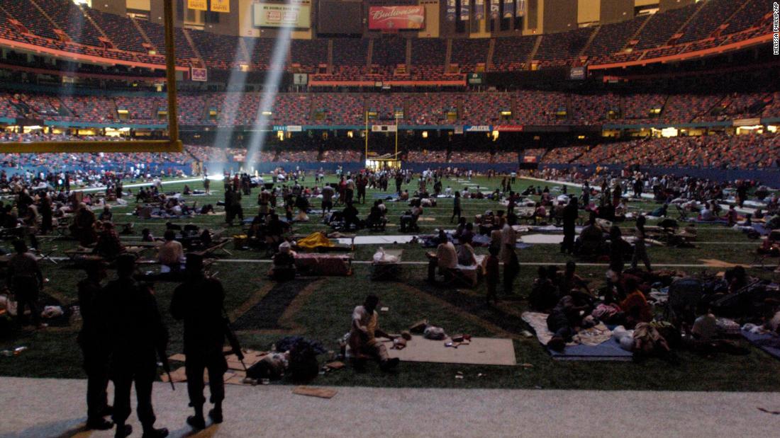 Members of the National Guard, standing in the foreground, watch over evacuees who took shelter at the Superdome in New Orleans. The shaft of light came from a hole in the roof of the dome.