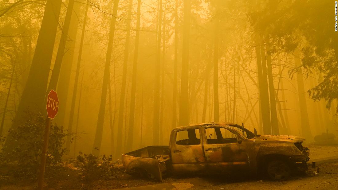 A burned-out vehicle is left in front of a destroyed residence as smoke fills the sky in Boulder Creek on August 22, 2020.
