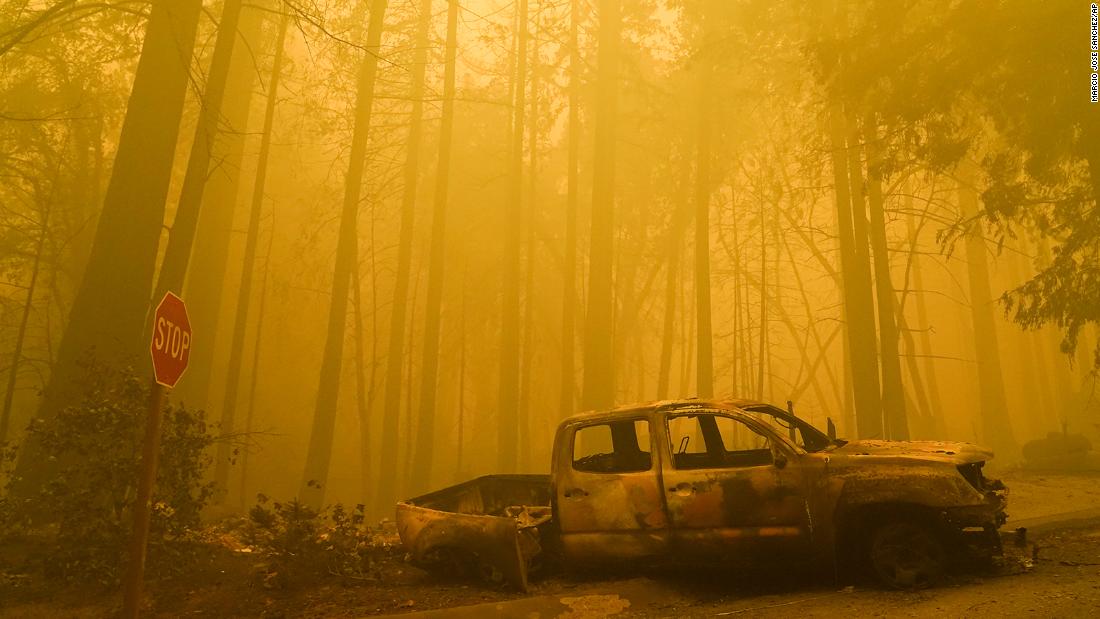 A burned-out vehicle is left in front of a destroyed residence as smoke fills the sky in Boulder Creek on August 22.