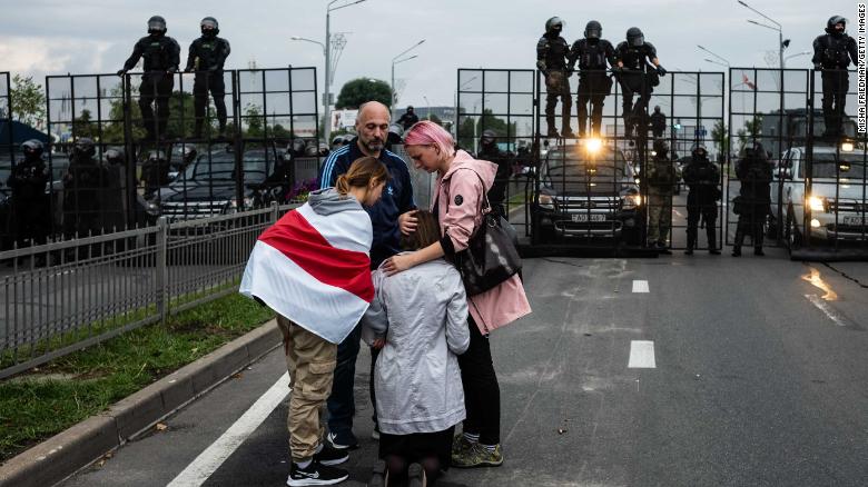 Anti-government protesters console a praying woman near riot police in Minsk on Sunday.