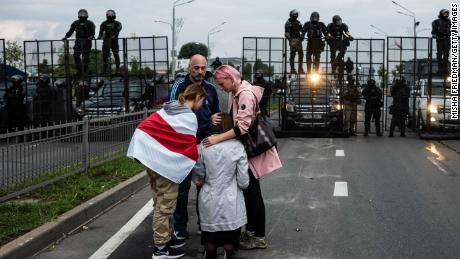 Anti-government protesters console a praying woman near riot police in Minsk on Sunday.