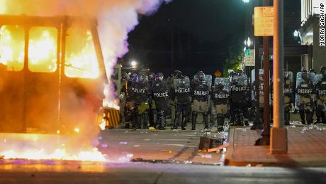 Police stand near a garbage truck ablaze during protests Monday in Kenosha