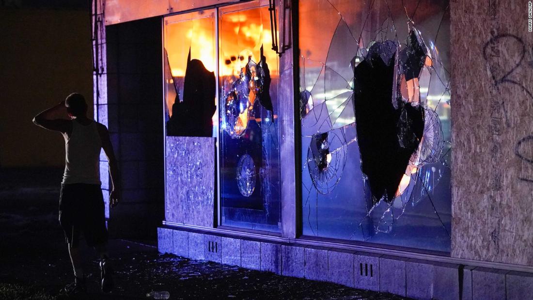 Burning structures are reflected in a building&#39;s broken glass as a protester walks past on August 24.