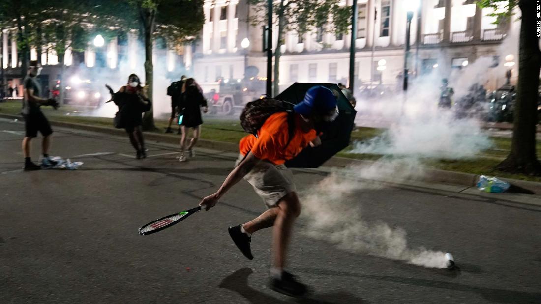 A demonstrator uses a tennis racket to return a tear-gas canister toward police lines.