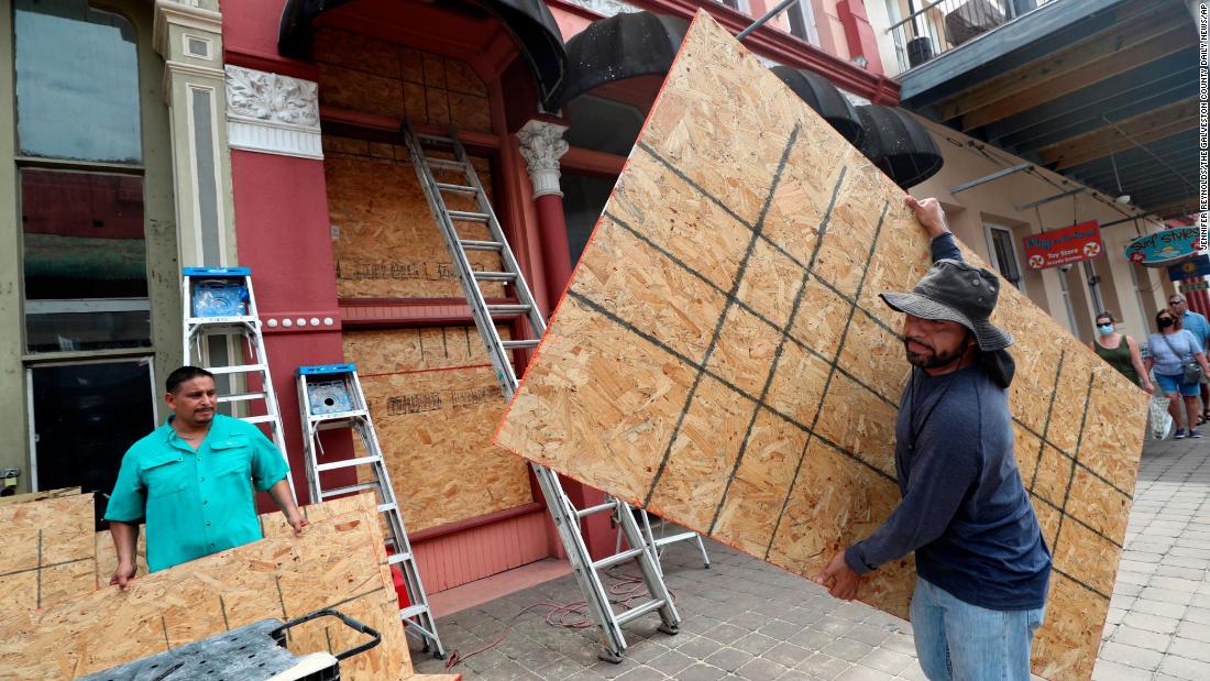 Cesar Reyes, right, carries a sheet of plywood as he helps install window coverings at a business in Galveston.