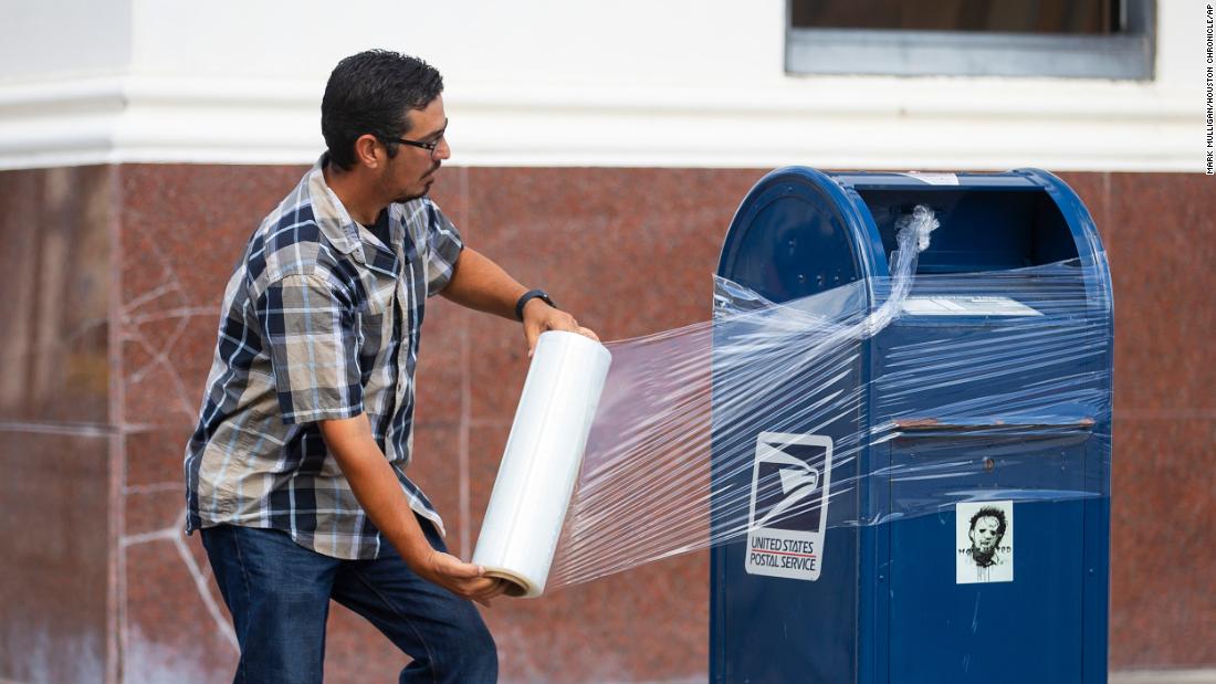 A US Postal Service employee covers a mailbox with plastic wrap in Galveston, Texas. The plastic wrap signals that the final mail has been cleared from the box, and it prevents people from placing mail inside that could be lost in a flood.
