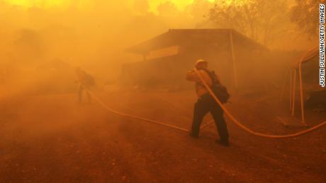 Firefighters carry a hose toward a burning structure as the LNU lightning complex fire burns near Napa, California.  This year, fewer inmates can help fight wildfires.