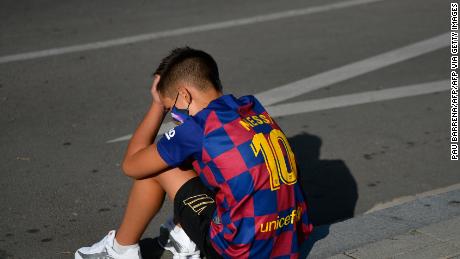 A disappointed young Barcelona supporter sporting Lionel Messi&#39;s jersey sits on the pavement outside the Barcelona training ground hoping for a glimpse of his hero.