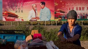 TURPAN, CHINA - SEPTEMBER 08: (CHINA OUT) An ethnic Uyghur woman arranges raisins for sale at her stall with a billboard showing the late Communist Party leader Mao Zedong in the background before the Corban festival on September 8, 2016 in Turpan County, in the far western Xinjiang province, China. The Corban festival, known to Muslims worldwide as Eid al-Adha or &#39;feast of the sacrifice&#39;, is celebrated by ethnic Uyghurs across Xinjiang, the far-western region of China bordering Central Asia that is home to roughly half of the country&#39;s 23 million Muslims. The festival, considered the most important of the year, involves religious rites and visits to the graves of relatives, as well as sharing meals with family. Although Islam is a &#39;recognized&#39; religion in the constitution of officially atheist China, ethnic Uyghurs are subjected to restrictions on religious and cultural practices that are imposed by China&#39;s Communist Party. Ethnic tensions have fueled violence that Chinese authorities point to as justification for the restrictions. (Photo by Kevin Frayer/Getty Images)