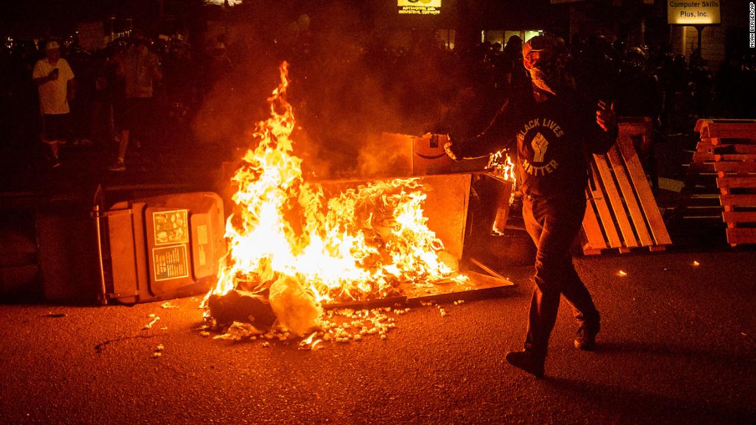 A protester passes a dumpster fire in Portland, Oregon, on Saturday, September 5. Saturday marked the 100th night of protests in the city since the death of George Floyd in late May.