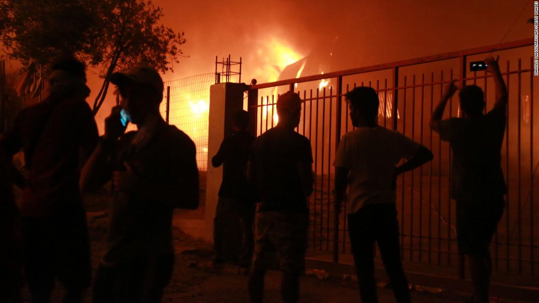 Migrants stand outside the Moria camp as it burns.