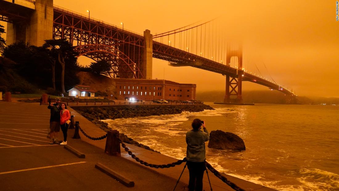 People stop to take pictures of the Golden Gate Bridge as it is affected from smoke by nearby wildfires on September 9.