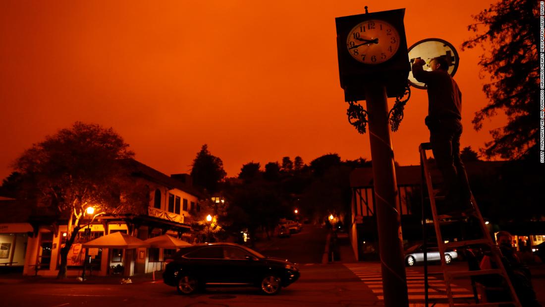 Bejhan Razi, a senior building inspector in Mill Valley, California, checks out repairs on a lamp-post clock as the sky is illuminated by nearby wildfires.