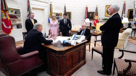 In this White House photo from December 2019 provided by Bob Woodward, President Donald Trump is seen speaking to Woodward in the Oval Office, surrounded by some aides and advisers, as well as Vice President Mike Pence. On Trump&#39;s desk is a large picture of Trump and North Korean leader Kim Jong Un.