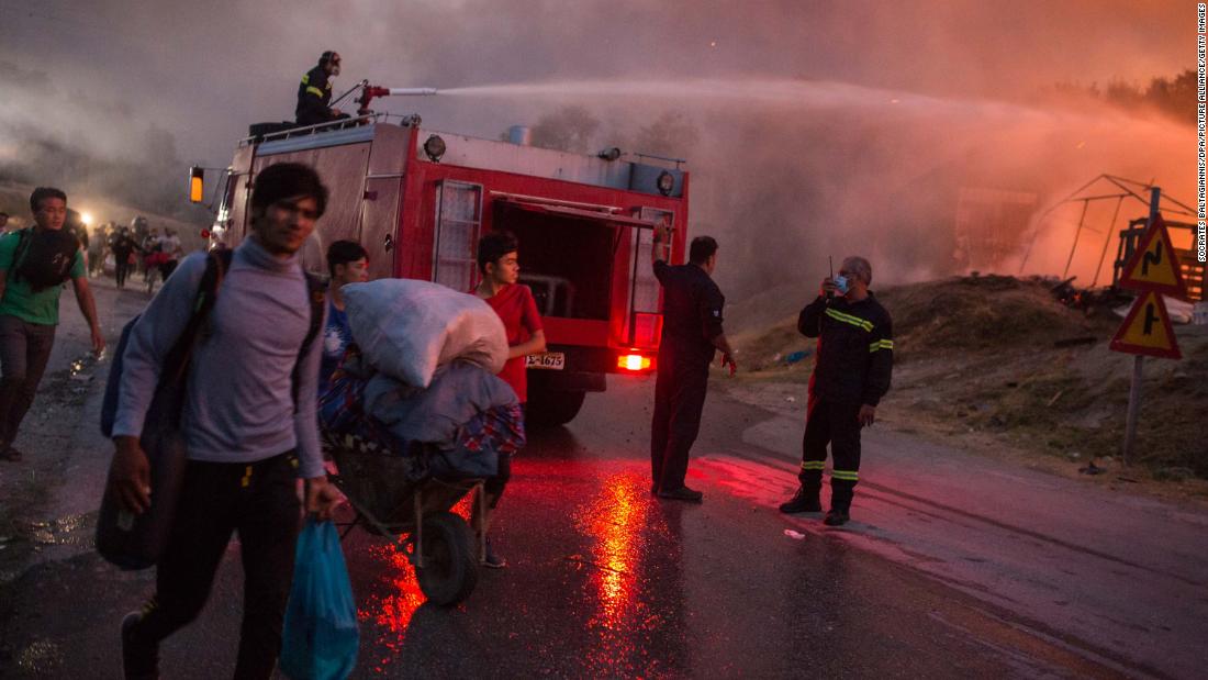 People evacuate the camp with their belongings as firefighters work to extinguish the blaze.