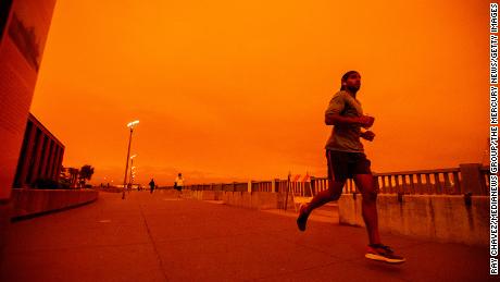 People jog along Embarcadero as smoky skies from the northern California wildfires casts a reddish color during the morning in San Francisco, Calif., on Wednesday, Sept. 9, 2020.
