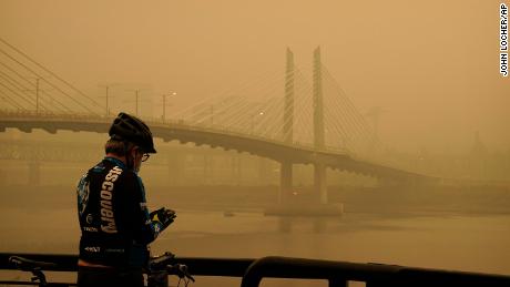 A man stops on his bike along the Willamette River as smoke  partially obscures the Tilikum Crossing Bridge on Saturday in Portland, Oregon.