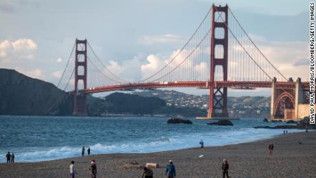 People walk at Baker Beach in March as the Golden Gate Bridge stands in the background in San Francisco.