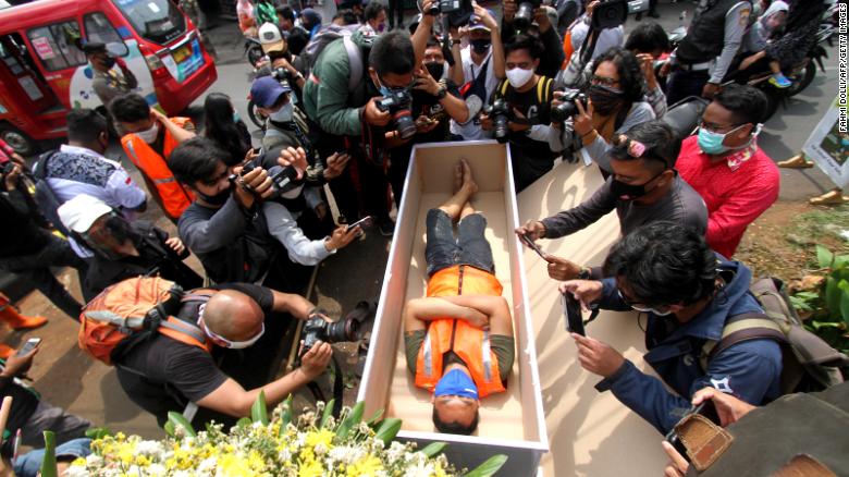 A man caught not wearing a face mask in public lies in a mock coffin while members of the public and the media take pictures as part of punishment by local authorities and enforced by local police in Jakarta on September 3.