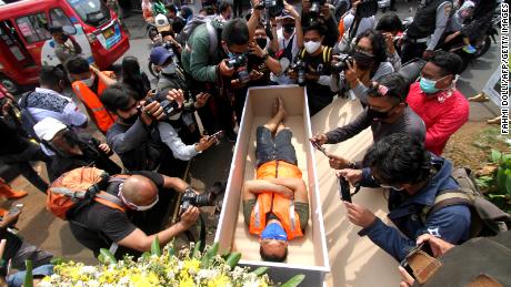 A man caught not wearing a face mask in public lies in a mock coffin while members of the public and the media take pictures as part of punishment by local authorities and enforced by local police in Jakarta on September 3.