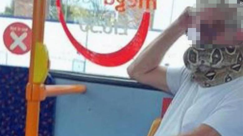 A man (seen here with his identity obscured) was photographed on a bus in the UK wearing a snake as &quot;face mask.&quot;