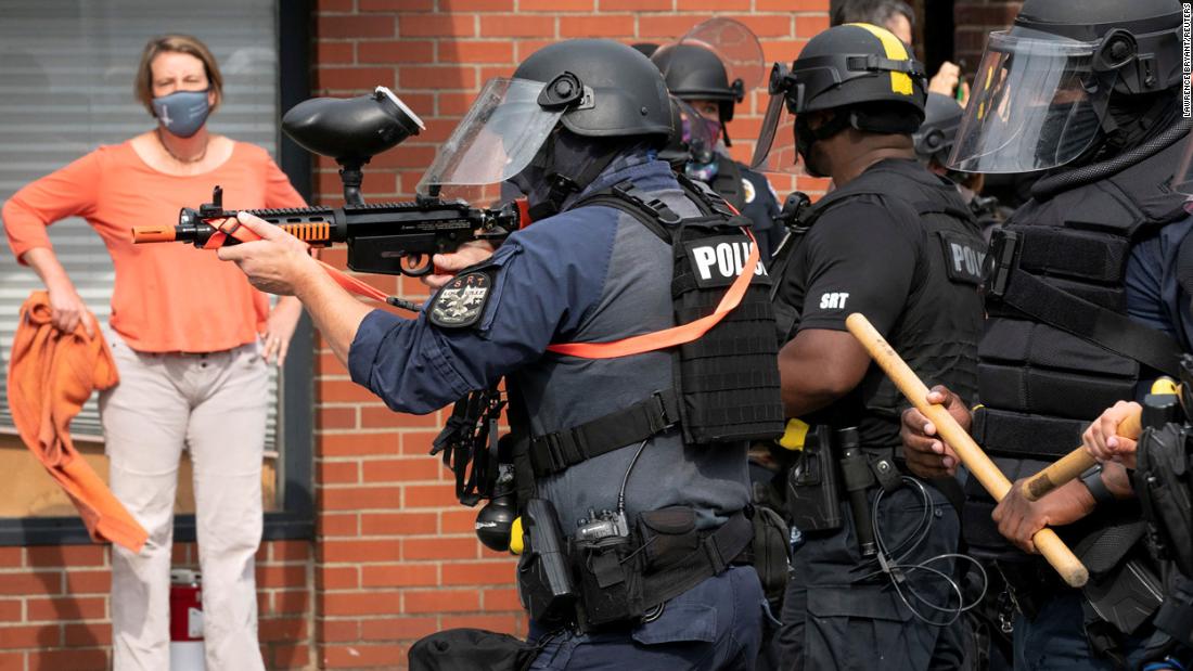 A Louisville police officer fires a pepper ball gun into a crowd of protesters.
