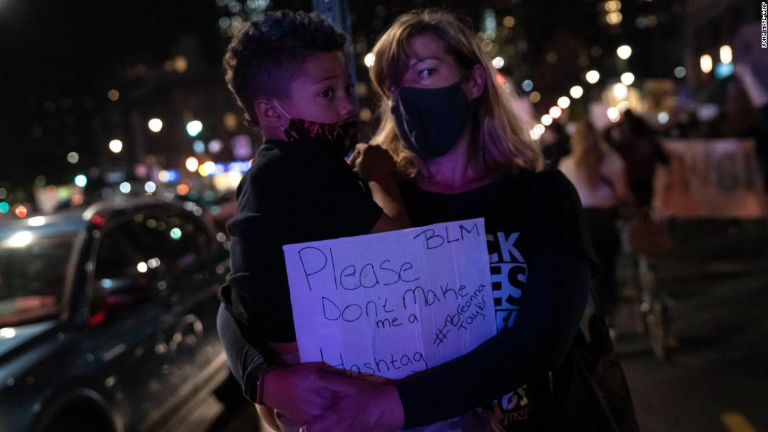 A woman carries a boy and a sign that reads, &quot;Please don&#39;t make me a Breonna Taylor,&quot; as they watch protesters gather in Brooklyn, New York.