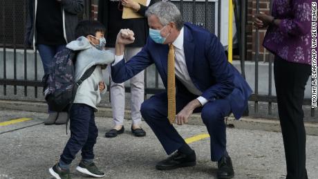 New York City Mayor Bill de Blasio does a welcome elbow bump with a pre-K student in Queens. The mayor has pushed for schools to resume in-person tuition.