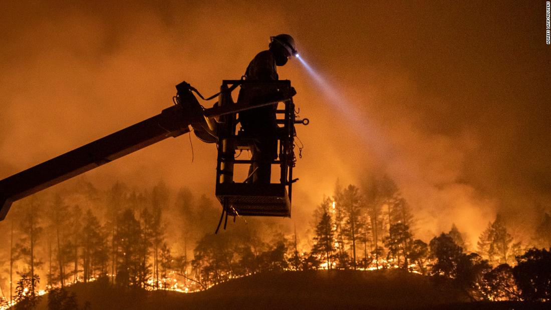 The Glass Fire burns in the background as Josh Asbury, an employee of CableCom, installs fiber-optic cable in Calistoga on September 28, 2020.