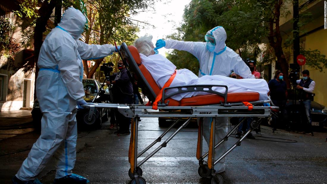 A paramedic adjusts a patient&#39;s face mask outside an Athens, Greece, nursing home where dozens of people tested positive for Covid-19.