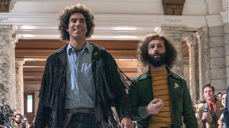 "Abbie Hoffman" (Sacha Baron Cohen) and "Jerry Rubin" (Jeremy Strong) walk down a courthouse hallway lined with reporters in "The Trial of the Chicago 7."